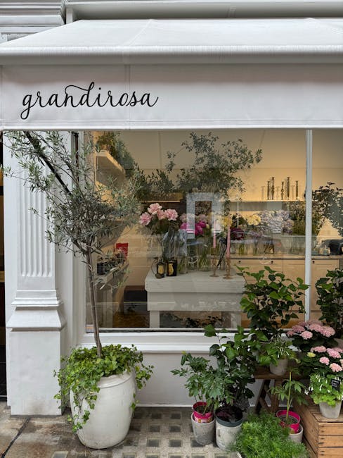 The image shows the exterior of a florist shop named 'grandirose' with a large glass window display. Inside, there are arrangements of fresh flowers, predominantly pink and white, placed on tables and